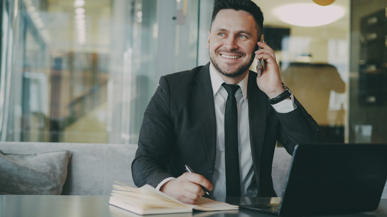 Smiling businessman making a phone call while working in a modern office environment.